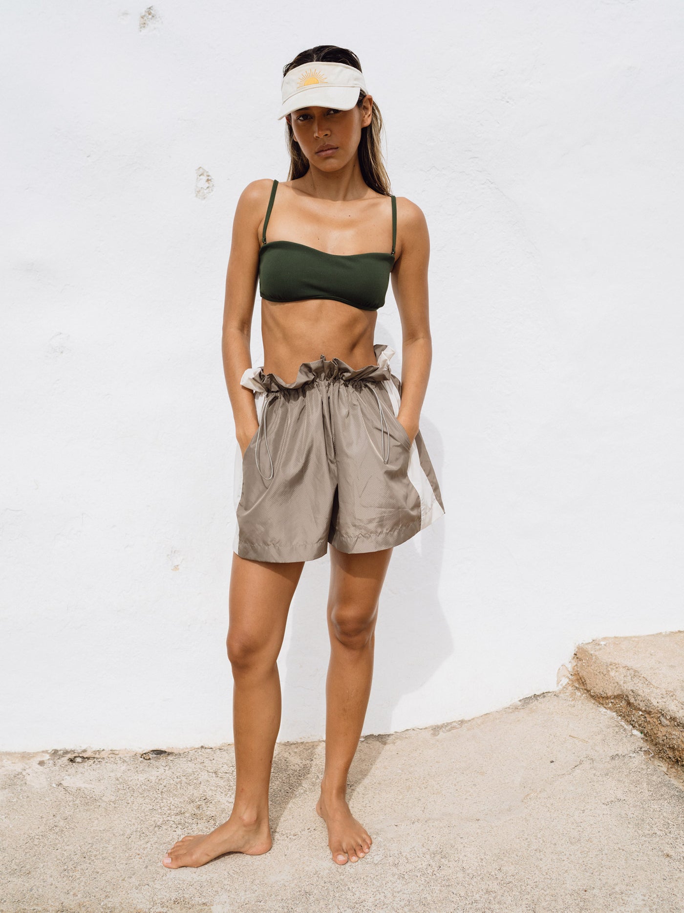 A girl wearing Track Shorts in a sunny environment, paired with a bikini top and sun visor. The shorts, made from comfortable and fast-drying material, feature stylish color-blocking in grey and creme and an oversized fit for versatile activities. The adjustable waist adds both style and comfort.